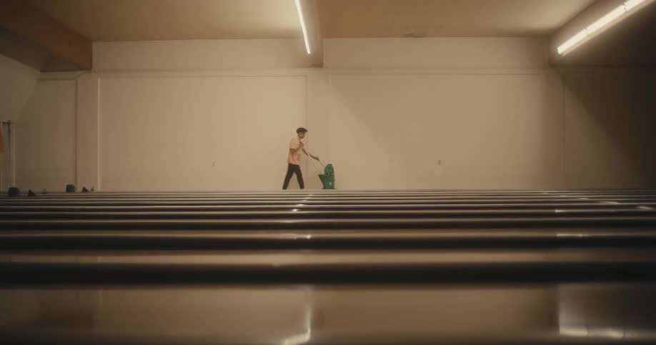 A man walks wheeling a mop and bucket past the bowling alley lanes