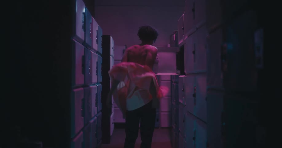 Young black man standing in a locker room taking his shirt off and putting it in a locker