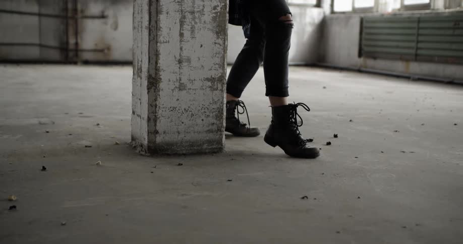 A woman wearing boots dances near a pillar in an empty room