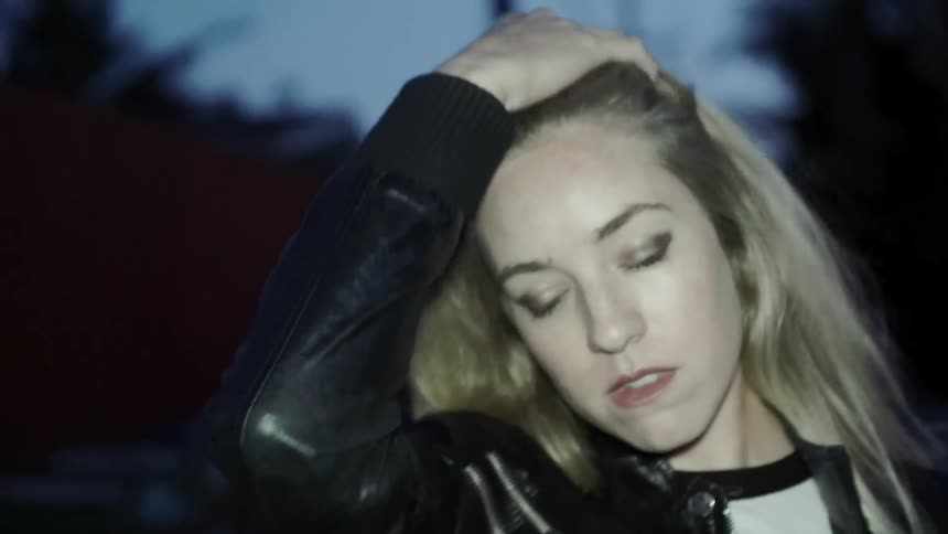 A blond woman in a black jacket walks at night