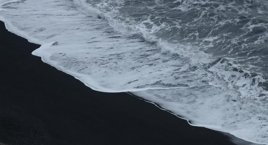 Waves wash ashore on a beach with black sand