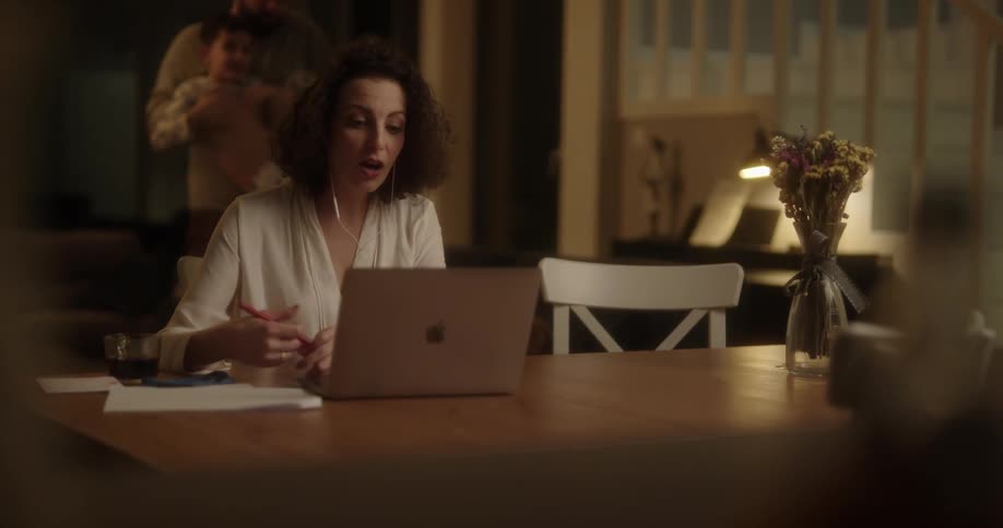 Mother sitting at the table on a video call on her laptop and then screaming to the father and son that were playing in the couch making them leave the room