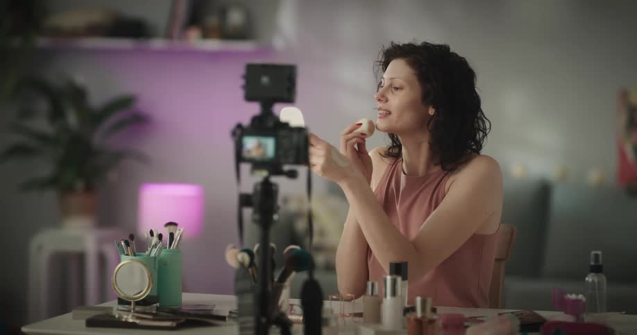 Young white woman applying makeup and recording herself with a photography camera