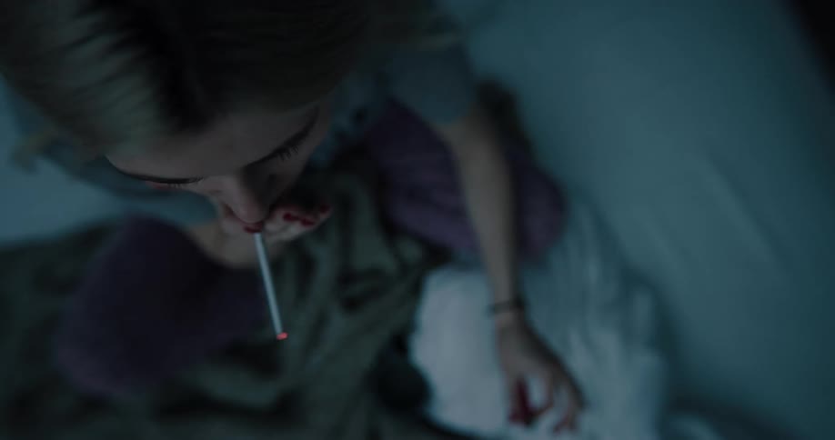 Young white woman sitting on the bed lighting a cigarette and smoking