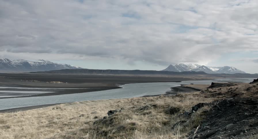 A stream is running through a field before some mountains