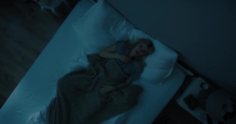 Blonde woman in gray t shirt lying in bed uses smartphone in bedroom at night