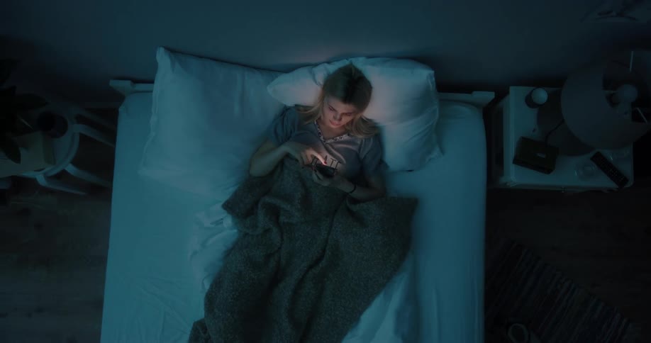 A woman is laying down and texting on a cellphone