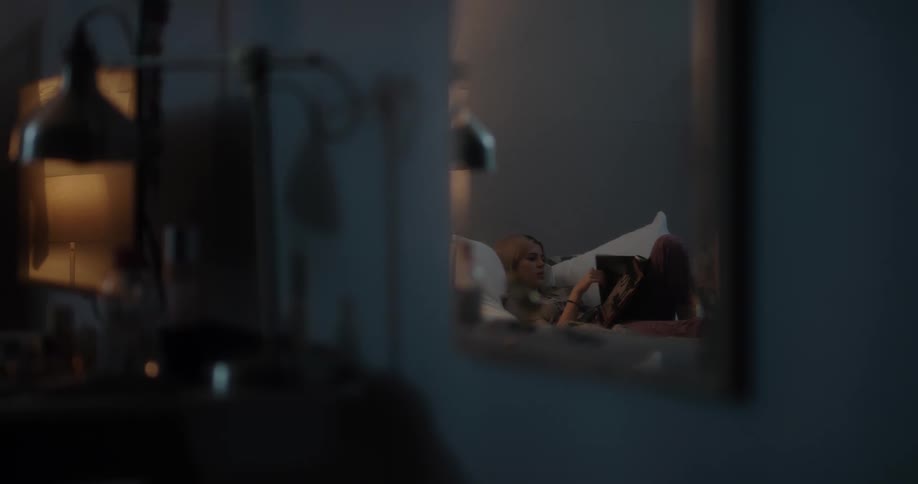 Mirror reflection of a young white woman lying in her bed and leafing through a magazine
