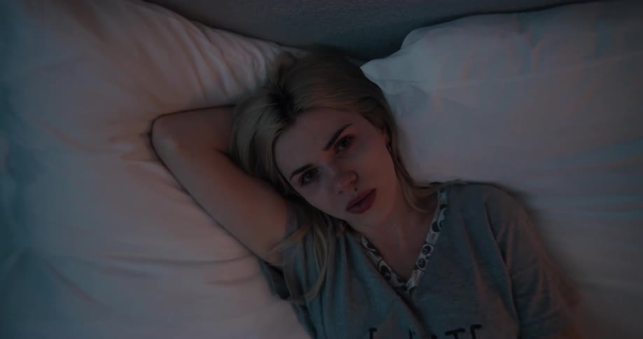 Young white woman using her smartphone while lying down in the bed with a sad looking face
