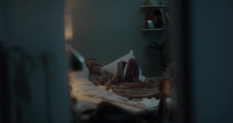 White young woman reading a magazine while shes lying down in her bed on her bedroom during night