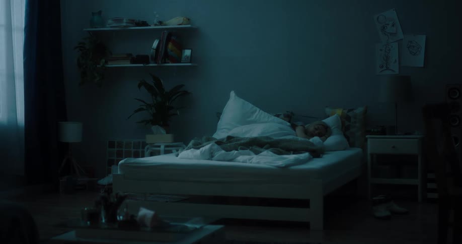 A woman lying in bed puts her legs under the covers and curls up to sleep