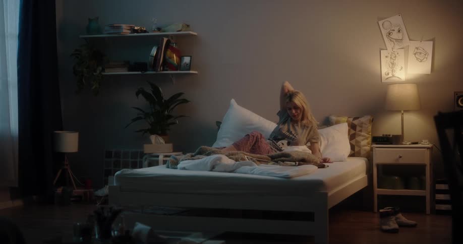Young blonde woman waking up in bed turns on the table lamp to read magazines