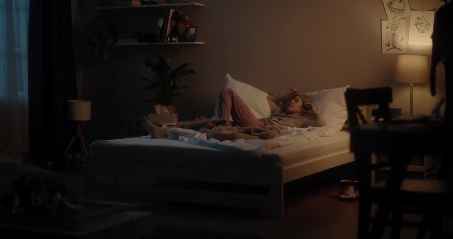 Young woman stops reading a magazine and readies to sleep over a bed in the bedroom at home