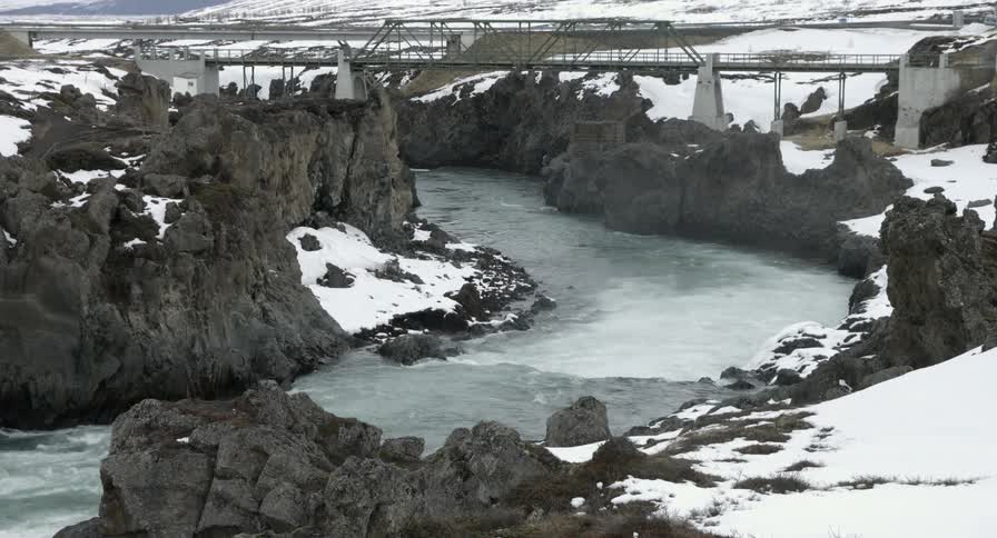 River surrounded by rocks and snow flows under a bridge