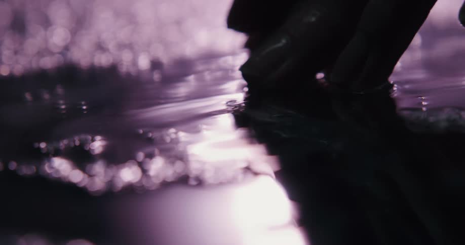 A person runs their fingers through a puddle outside