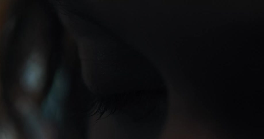 Close up of the closed eye of a woman inside a dark room in front of a shimmering background