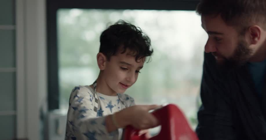 Young boy mixing batter with a hand mixer as his father watches