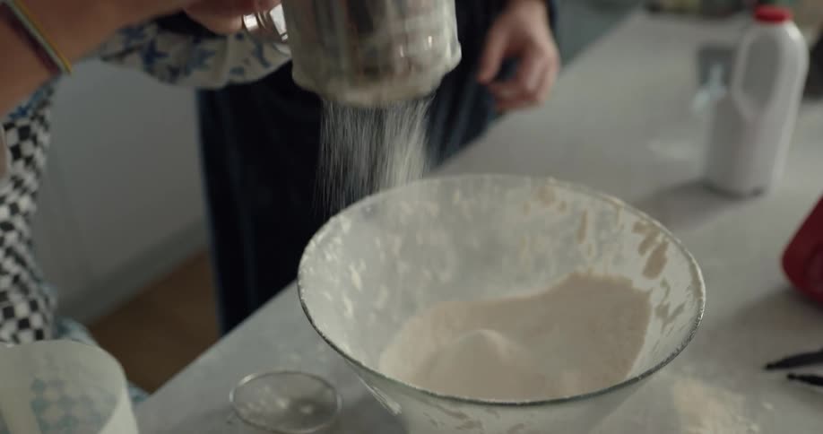A father helps a son put flour in a bowl as they cook together
