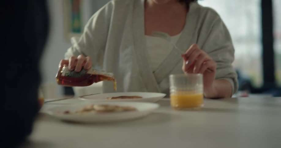 A woman talks with a man while eating pancakes at a dining table at home during the day