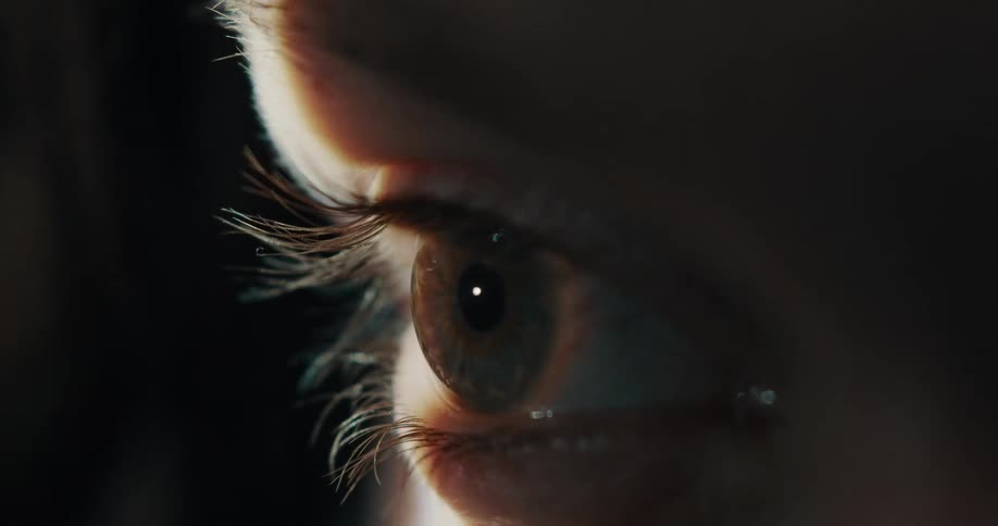 Close up of a ray of light passing over the open eye of a woman inside a dark room