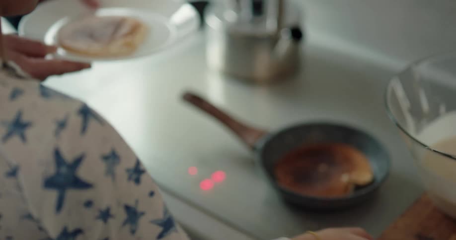 A boy flips a pancake in a pan as his dad stands beside him to help