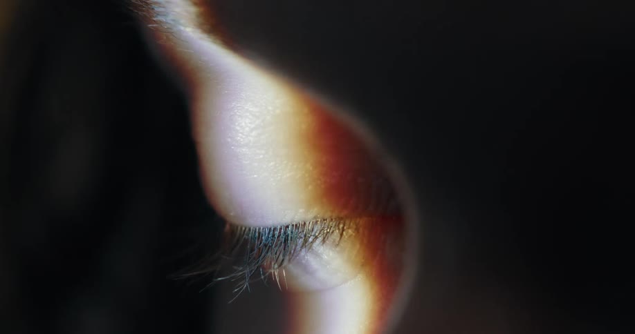 Close up of a ray of light passing over the open eye of a woman inside a dark room