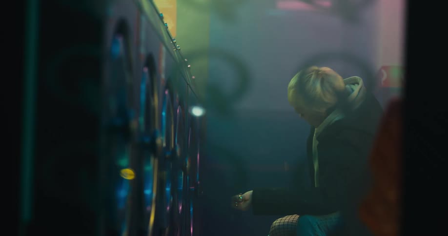 A woman runs her hands through her hair and checks her smartphone while waiting at a laundromat