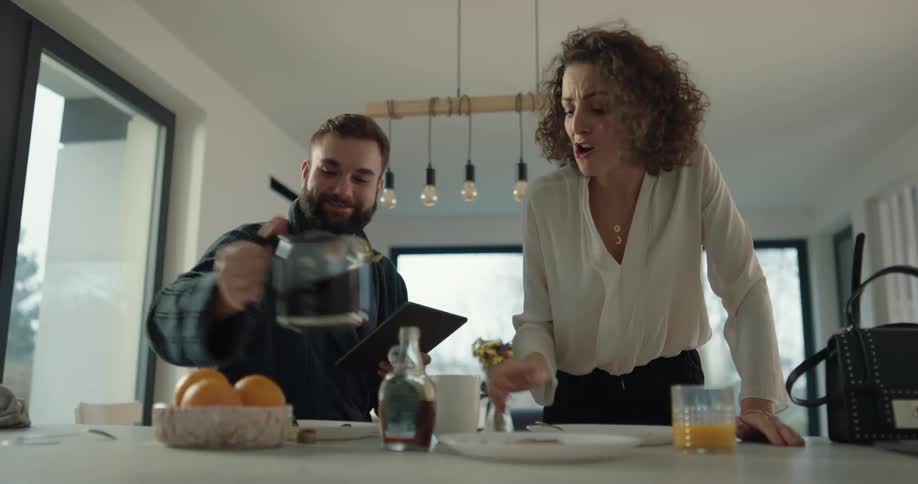 Husband helps his hurried wife to barely eat breakfast and kissing before leaving for work