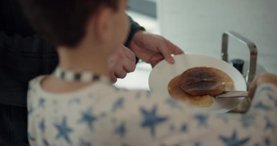 A boy places a just cooked pancake onto a plate held by a parent