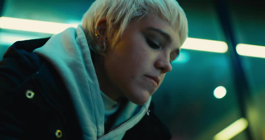 Young white woman sitting next to a big glass window leg bouncing and biting her nails in a very anxious way