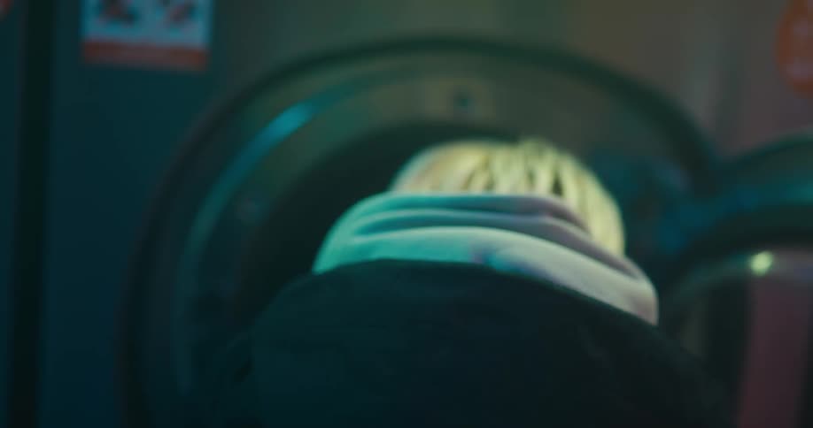 Blonde woman wearing a jacket and a hoodie putting clothes on a washing machine