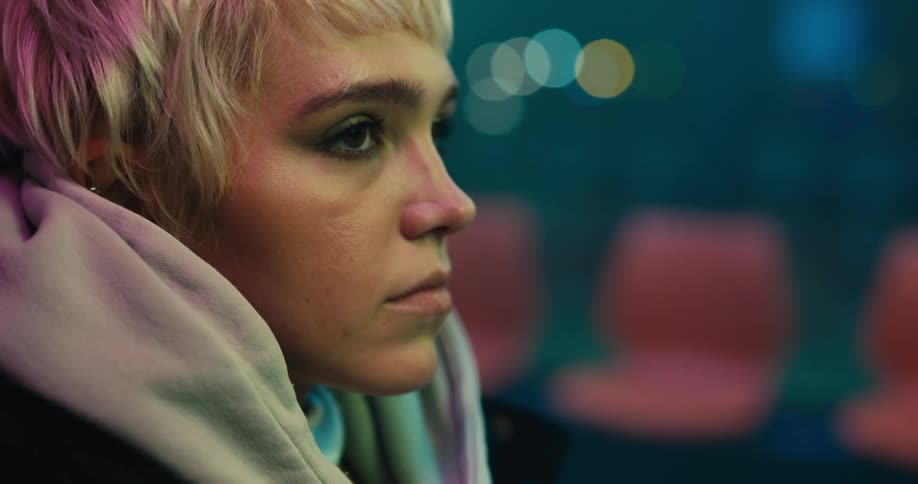 Young blonde woman sitting near a row of red seats on a laundromat at night