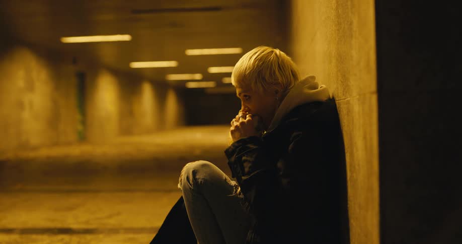 Young white woman sitting in the ground inside a concrete corridor eating a sandwich