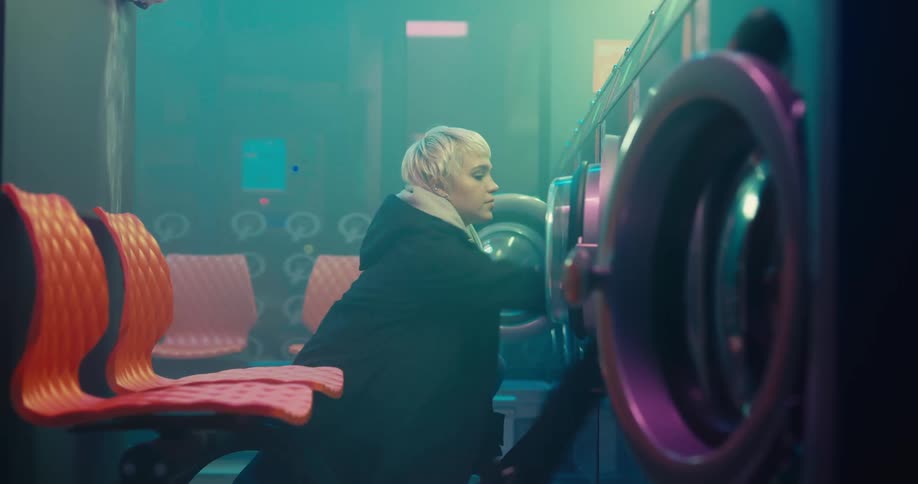 A woman loads a washer in a laundromat with her clothes while a car travels by at night