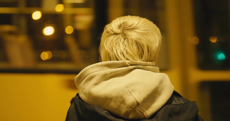 A teenage girl steps back and watches a subway go past her at night