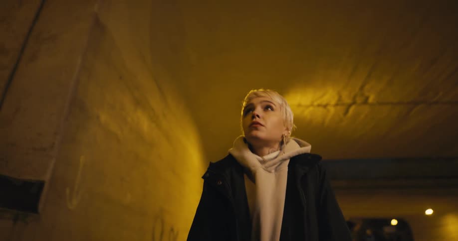 A nervous female teenager walking through a freeway underpass at night