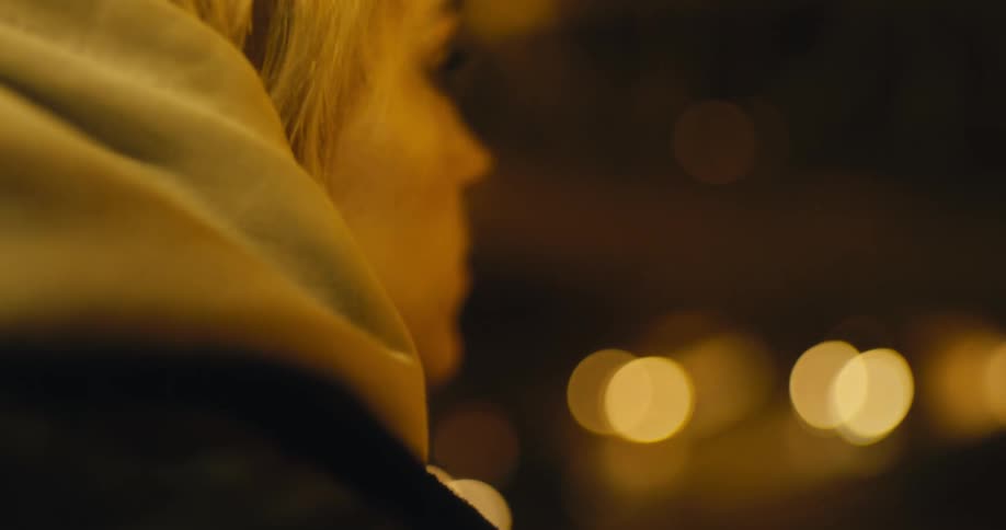 A woman is standing outdoors at night and wearing a coat