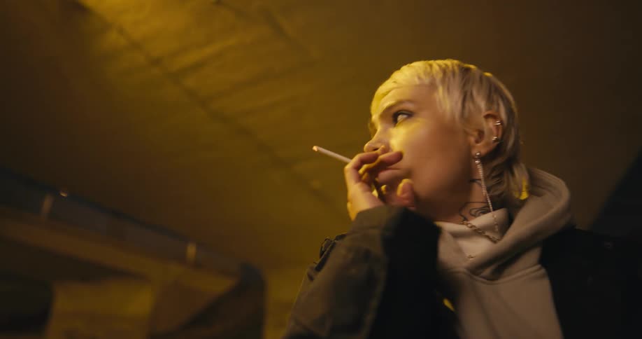 A woman smokes a cigarette while standing under a bridge
