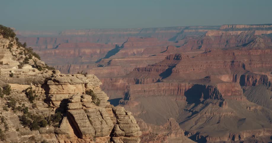 The sun shines brightly upon rock formations and mountains under a clear sky