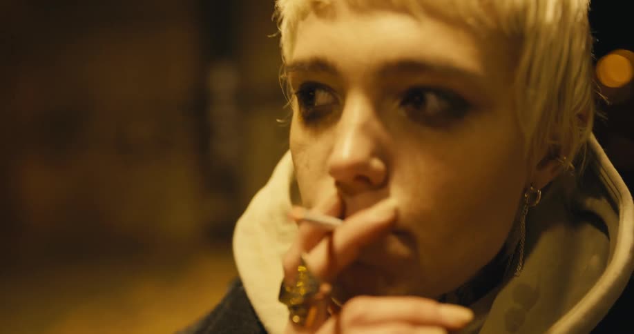 A young woman looks nervous as she smokes a cigarette outside on a cold night