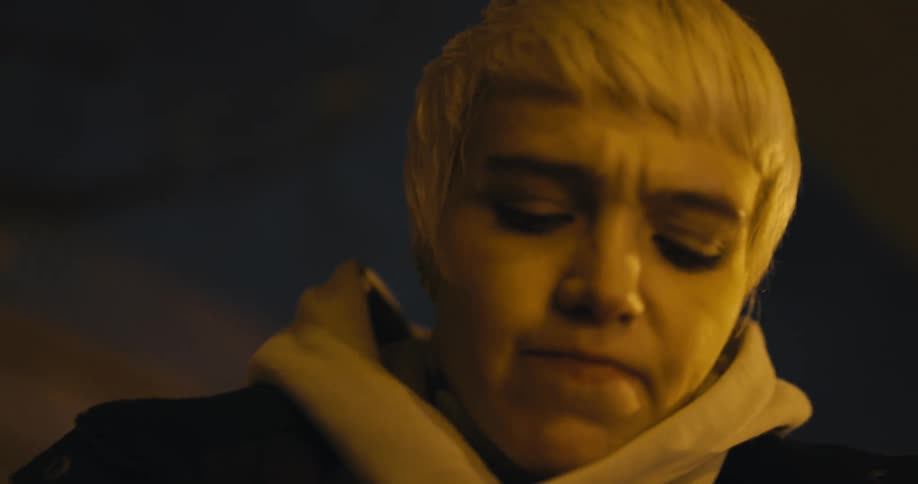 Blond teenager uses her cell phone as she looks around nervously at night