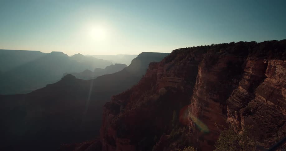 The sun shines brightly upon mountains and rock formations with silhouettes of mountains on the horizon