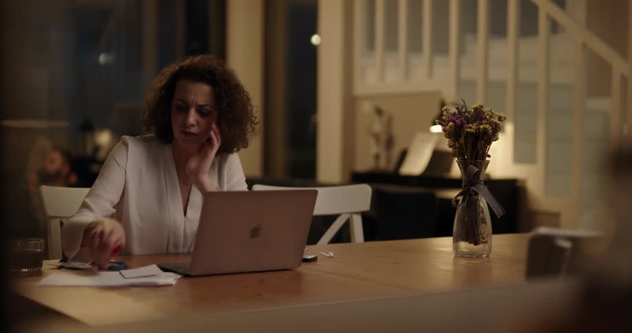 A frustrated woman working on her laptop at night on her dining table