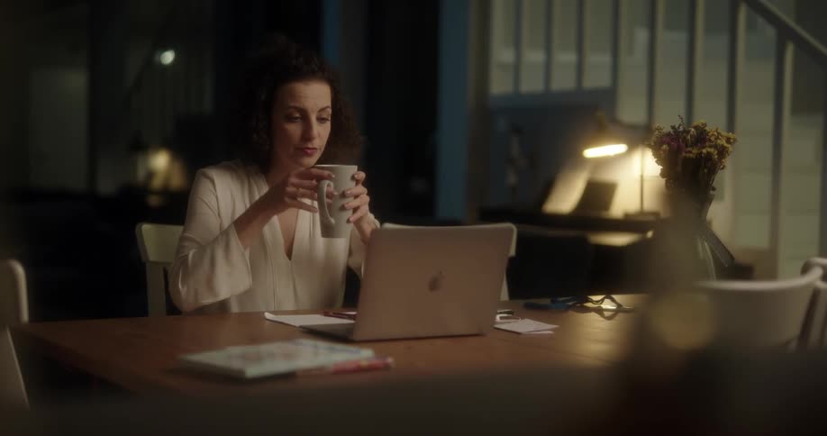 Woman writes on a paper then drinks from a mug and closes a laptop