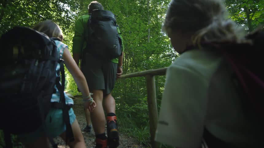 A family hikes across a narrow pedestrian bridge in the forest