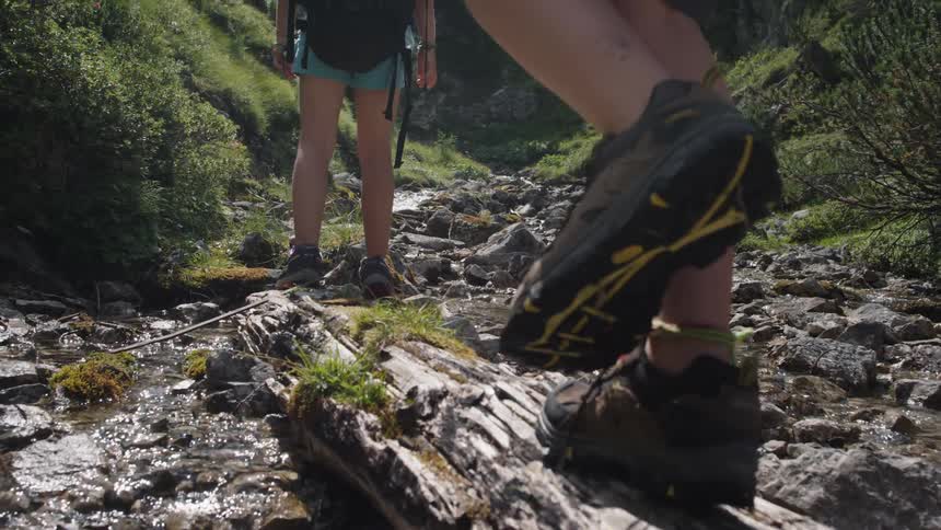 Person walking over a log on a shallow river in the mountains while hiking
