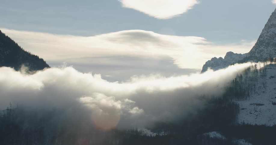 Clouds and fog roll over mountain slopes and trees on a bright day