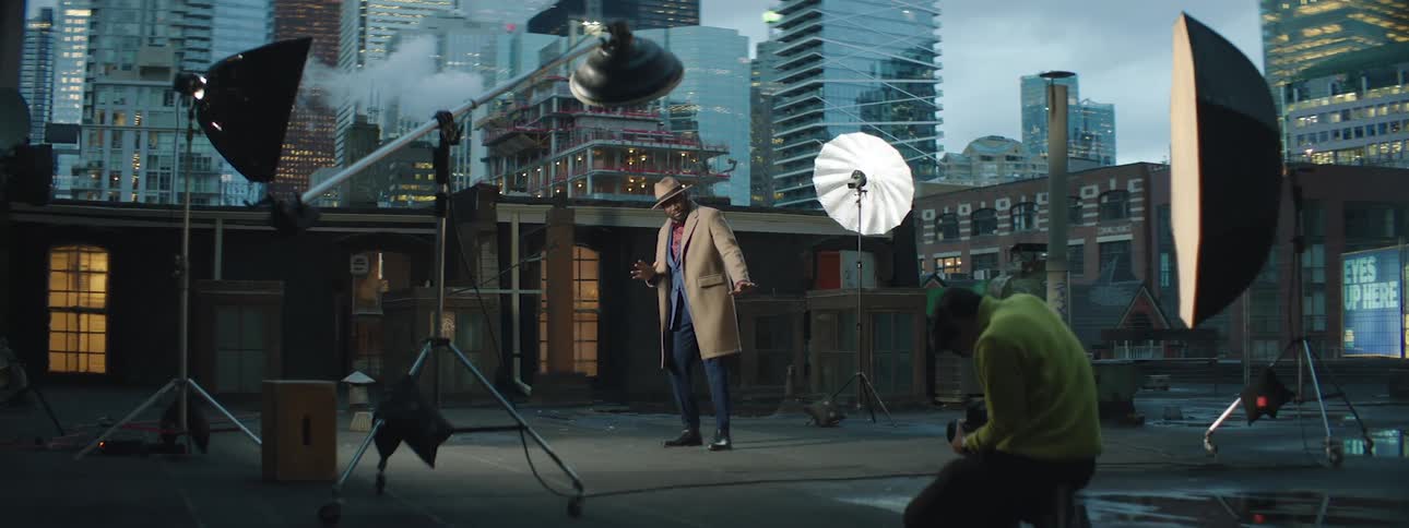 A man strikes a couple of poses at a professional photo shoot on a rooftop with the city skyline behind him