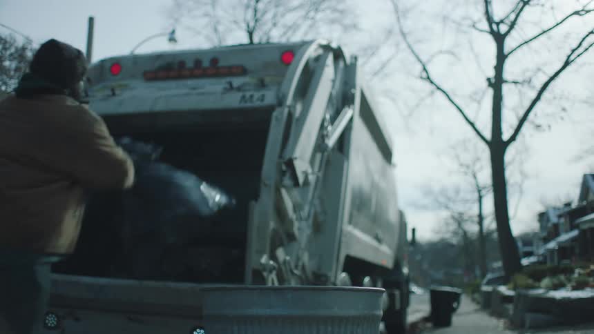 A man is working for a garbage truck in a neighborhood