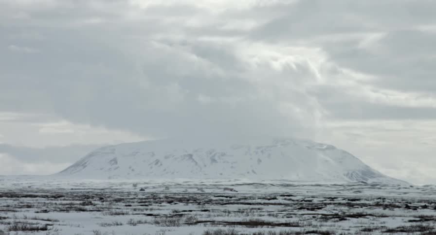 A tall, snowy crater under thick white clouds